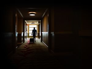 Young man walking with rolling suitcase thru a creepy corridor