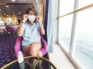 Young woman putting on a protective face mask to travel safely on a cruise ship, Mediterranean sea, Italy